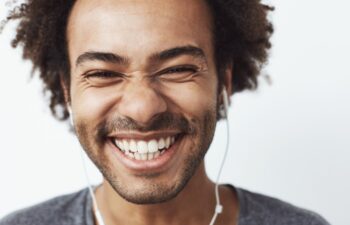 Close up portrait of young happy african man smiling listening to upbeat streaming music laughing over white background. Youth concept. Copy space.