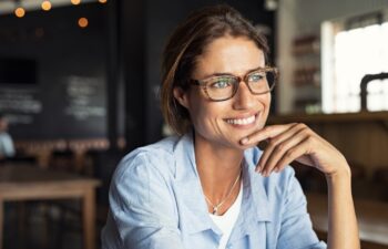 Portrait of beautiful mature woman sitting in cafeteria looking away. Cheerful mature woman wearing eyeglasses thinking with finger on chin. Happy woman relaxing at cafe and smiling.