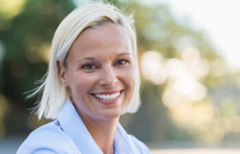 Portrait of mature woman smiling and looking at camera outdoor. Closeup face of a middle aged woman smiling at park. Blond mid woman relaxing in the lawn in a summer day.