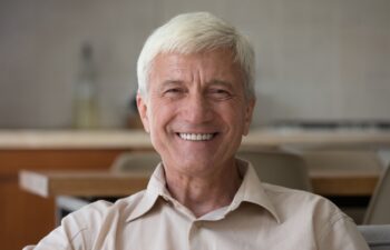 Head shot portrait handsome optimistic senior man sit indoor looking posing on camera, having wide toothy smile advertise professional dental clinic services for elders. Carefree retirement concept