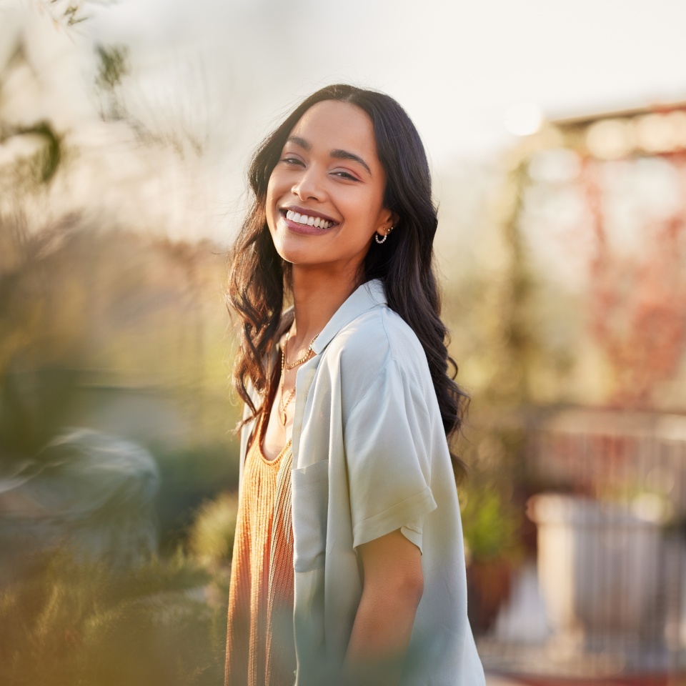 Young latin woman in casual clothing in the garden looking at camera, during early morning. Portrait of healthy mexican girl enjoying nature during sunset. Mindful multiethnic woman enjoy morning.