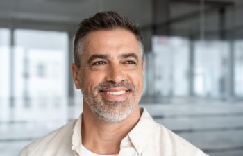 Headshot close up portrait of indian or latin confident mature good looking middle age leader, ceo male businessman on blur office background. Handsome hispanic senior business man smiling aside.