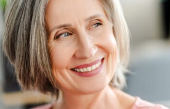 Closeup portrait smiling confident senior woman sitting on comfortable sofa at home. Happy retired female with stylish gray hair, white teeth looking away. Natural beauty, healthy lifestyle concept