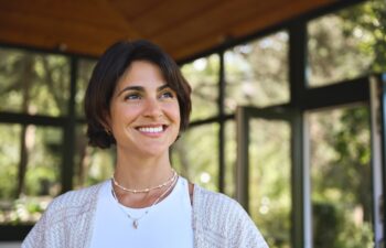 Young happy confident Hispanic woman health coach, yoga instructor, holistic teacher looking away standing in yoga studio advertising retreat mind body health therapy classes. Copy space.