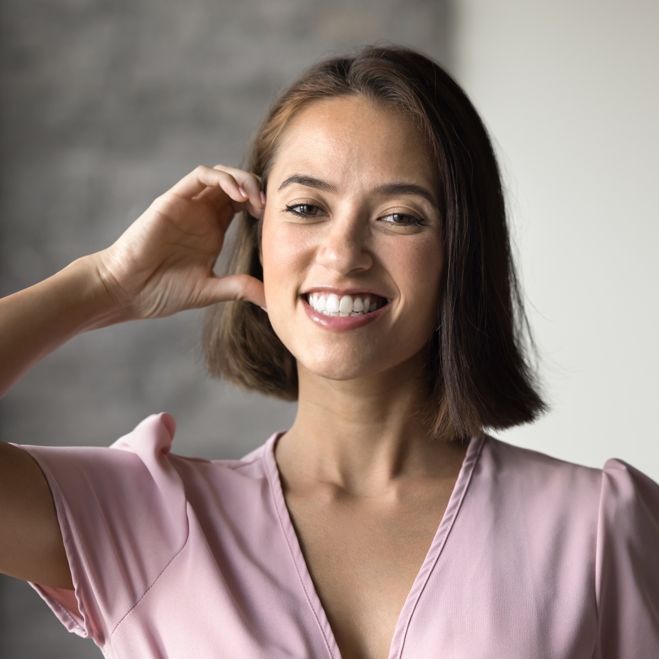 Happy beautiful young adult girl touching face with half-heartedly fingers, making half heart hand, gesture of love, happiness, symbol of romance, beauty, kindness, looking at camera for portrait