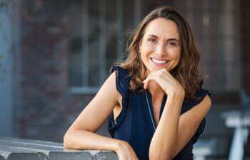 Portrait of beautiful mature woman sitting at coffee shop. Happy hispanic smiling woman sitting on a bench in outdoor cafeteria looking at camera. Portrait of carefree woman relaxing on bench.